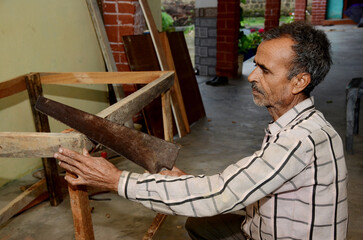 Indian old man working in a wood workshop with a saw