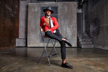 Contemporary African American man, actor or dancer sits on a stool on stage, dressed in a red shirt...