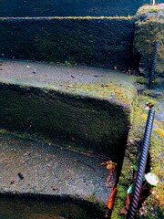 Gros plan de marches d'escalier et de pierre historique, avec de la mousse végétale poussant de partout, sous un effet photographique et macro, mouillé, temps de pluie, barre de fer infrastructure