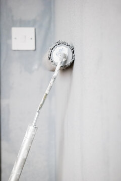 Paint roller extendable pole over painted woodchip wallpaper wall during home renovation in england uk
