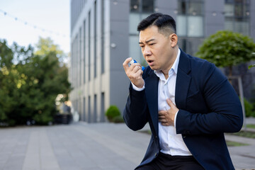 A young Asian man suffering from cough and asthma in a business suit is sitting near an office...