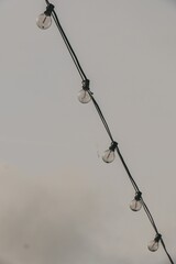 Vertical grayscale shot of string lights against a cloudy sky