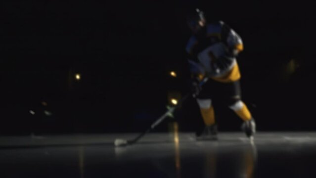 Ice hockey forward is skating and slides puck with his stick Player warms up before start of match on Ice arena with lights off Workout. Protective gear equipment. Blurred