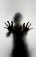 Eerie silhouette of a person with an outstretched hand behind textured glass