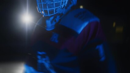 Ice hockey goalie goaltender warms up before game Workout butterfly drill exercise. Goalkeeper stretches his legs at goal. Protective gear equipment. Blue light. Ice arena with lights off - Powered by Adobe