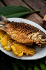 Vertical shot of a cooked whole fish and fried plantains on a plate