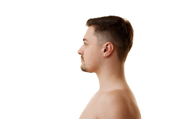 Naklejka premium Side view portrait of shirtless young man with brunette hair and stubble posing half-naked against white studio background. Concept of natural beauty, male health, anti-aging, spa procedures.
