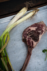 Piece of raw beef steak on a bone with green onion and spices from above