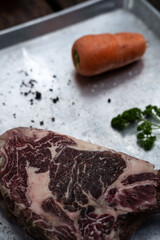 Piece of raw beef steak on a bone with carrot and spices from above
