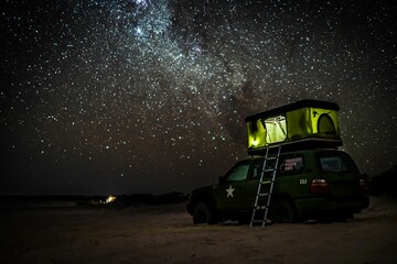 Gorgeous view of a camping truck with a ladder leading to a ten above it under a glowing night's sky