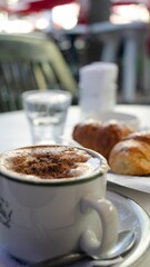 Vertical close-up shot of a cup of cappuccino and croissants on the breakfast table in cafe.
