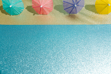 Abstract beach with glitter paper sand and water and cocktail umbrellas. Summer aesthetic mockup template background on a tropical beach holiday