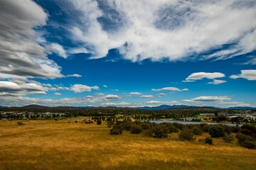 Fototapeta premium Scenic view of a field with trees and a lake in blue, cloudy sky background in a rural area