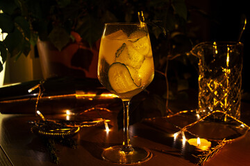 Closeup of a cucumber gin tonic cocktail in a wine glass decorated with candles and lights