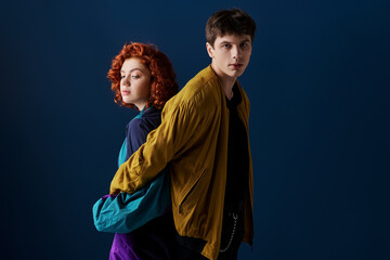 alluring woman posing back to back with her boyfriend who looking at camera on dark blue backdrop