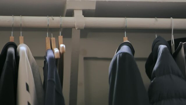 Person removing empty hanger from clothing rack inside closet. Grabbing a new hanger