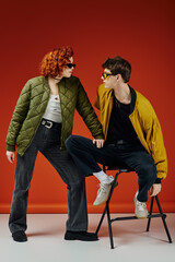 young man in fashionable attire with sunglasses sitting on chair next to his red haired girlfriend