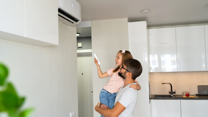 Happy family father and child adjust comfortable temperature of air conditioner using remote...