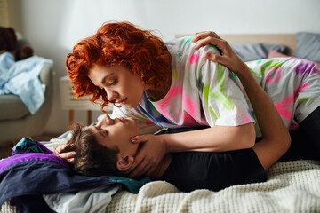 delighted young couple in comfy homewear preparing to kiss seductively while lying on bed together - obrazy, fototapety, plakaty