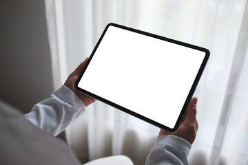 Mockup image of a woman holding digital tablet with blank desktop screen while sitting on a sofa at home