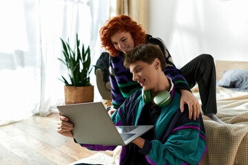 beautiful joyful woman in cozy attire sitting on bed and spending time with her boyfriend at laptop