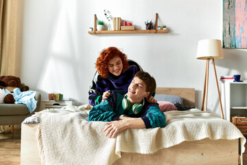 attractive man with headphones lying in bed with his appealing red haired girlfriend at home - obrazy, fototapety, plakaty