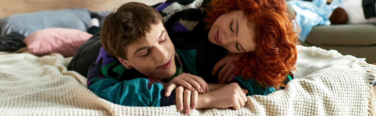 handsome man relaxing in bed next to his red haired alluring girlfriend while at home, banner