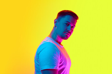 Portrait of confident young man with serious facial expression looking at camera in neon light...