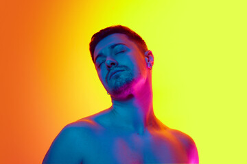 Portrait of young handsome half-naked man posing in neon light against vibrant yellow studio...