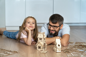 Father and child build wooden construction kit at home. Happy family play with construction set....