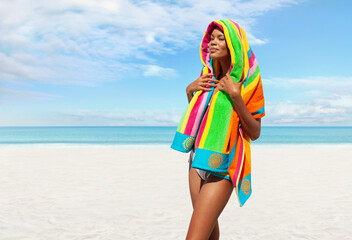 Woman at the beach side wrapped in a colorful towel, African latin American woman enjoying a sunny day with blue sky. Concept of summer beach holiday or booking travel and resort accommodations