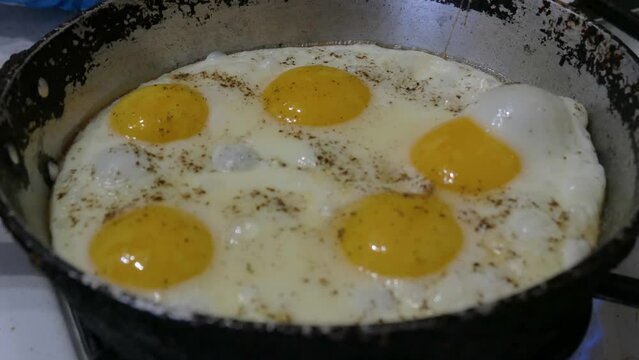 Cooking breakfast on a gas stove in the kitchen.  Cracked chicken egg in a frying pan. Eggs frying in an old frying pan in close-up.