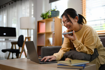 Smiling asian female freelancer having phone conversation and using laptop on sofa