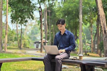 Portrait of young businessman working with laptop in the public park on sunny summer day