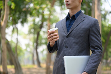 Millennial businessman drinking takeaway coffee during walking in the public park