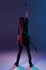 Energetic musician with long dreadlocks performing solo on stage against dark purple background in...
