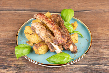 Freshly baked pork ribs with potatoes and seasonings on a plate with basil leaves.