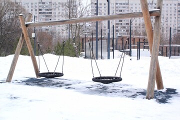 Wooden playground made of natural eco-friendly material in public city park with snow at winter time. Modern safety children outdoor equipment. Winter activities. Children rest and games on open air