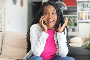 Excited african american woman with dreadlocks talking at phone indoors at living room