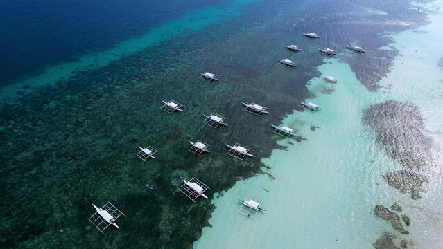 Aerial shot of fishing boats floating above coral reef in clear blue sea. Fishermen's boats in Philippines. Panglao island