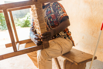 A blind man is sitting on a wooden bench and working on a piece of furniture - Powered by Adobe