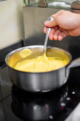 Hand stirring a creamy yellow mixture in a stainless steel pot on a stove, capturing the process of cooking