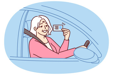 Happy elderly woman demonstrates driver license sitting behind wheel of car and rejoices at opportunity to go on road trip. Positive grey-haired old lady got driver ID after retirement - obrazy, fototapety, plakaty