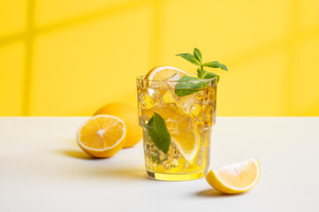 A glass of iced tea with lemon and mint on a yellow and white background with a shadow from the window.
