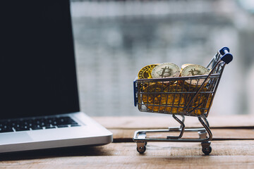 Shopping cart filled with piles of cryptocurrency bitcoin coins with computer laptop nearby on...