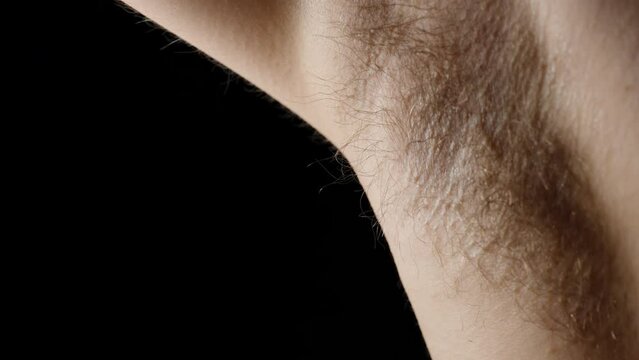 A man raises his hand and generously sprays deodorant under his hairy armpit. Close-up. Slow motion.