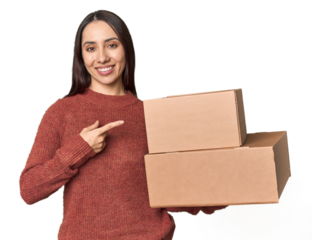Caucasian young woman with moving boxes on studio background smiling and pointing aside, showing something at blank space.