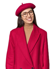 Fototapeta premium Stylish young Caucasian woman in red trench coat and beret on studio background happy, smiling and cheerful.