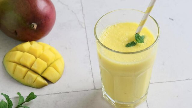 Man hand puts glass of yellow mango smoothie or milkshake with mint and straw on the table. Tropical healthy refreshment drink concept. Summer beverage