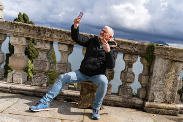 happy middle aged traveler man on vacation taking a selfie on an outdoor terrace facing lake Maggiore